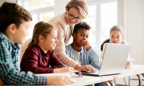 people in a government room with laptops and a teacher present